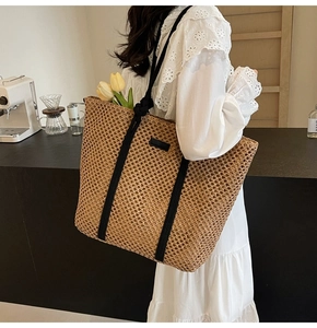 Close-up of woven straw tote bag featuring black fabric handles and a small side label