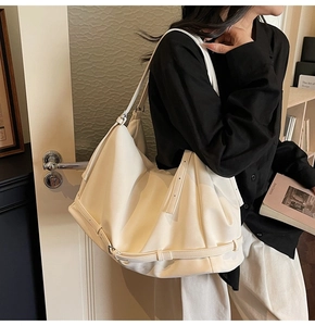 Detail of a large white slouchy tote bag with metal buckles on a fashion model