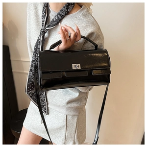 Detail of glossy black leather handbag with silver twist lock and decorative silk scarf
