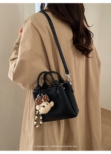Borsa in pelle nera con ciondolo a forma di orsetto indossata a tracolla dalla modella