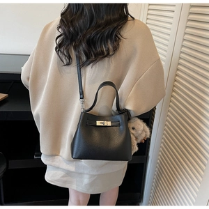 Detail of black lychee grain leather bucket bag featuring a gray plush bunny keychain