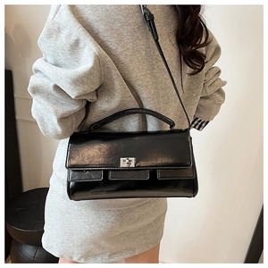 Detail of glossy black patent leather flap bag with silver twist-lock and top handle