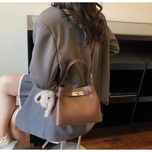 Detailed view of brown lychee grain leather handbag with gold twist lock and plush charm