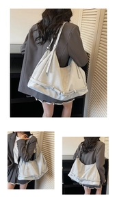 Detail of a large light grey soft leather hobo bag worn by a model in a grey suit