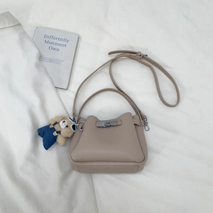 Detail view of beige pebbled leather bucket bag with silver twist lock and bear charm