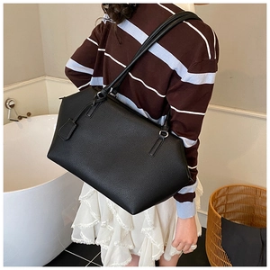 Close-up of black pebbled leather tote bag being worn by a model in a minimalist setting