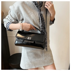 Close-up of black patent leather crossbody bag with silver twist lock and slim strap
