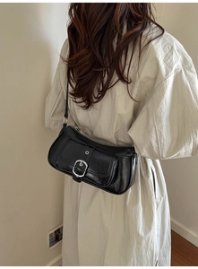 Detail of black faux leather baguette bag with silver buckle worn by a model in a dress
