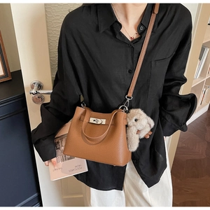 Close-up of brown litchi leather bucket bag with silver lock and plush bunny charm