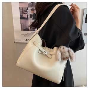 Detail of cream lychee leather bucket bag with metal turn-lock and plush bunny charm