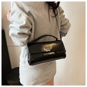 Detail of a black patent leather handbag with silver lock shown on a model