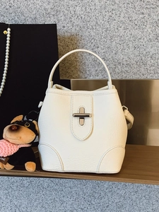 White lychee pattern leather bucket bag with metal clasp closure on a wooden shelf