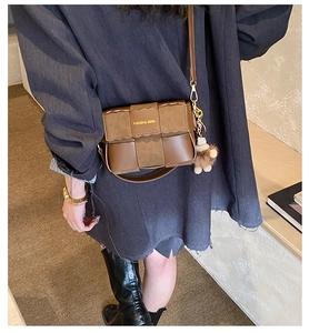 Detail of a brown woven PU leather crossbody bag with golden logo and plush bear charm