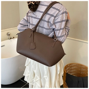 Detail of dark brown matte leather tote bag with shoulder strap worn by a model