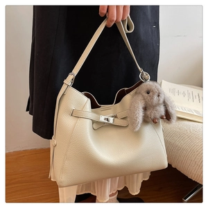 Close-up of beige lychee leather bucket bag with silver clasp and plush rabbit charm