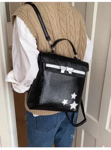 Detail of black glossy leather backpack featuring silver bow and star patches