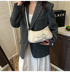 Detail of a chic cream-colored shoulder bag with a silver buckle worn by a model in a suit