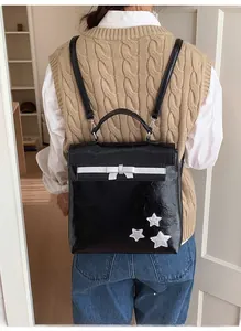 Model wearing a black glossy backpack with white bow and silver star accents in a cozy room
