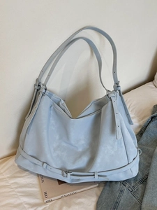 Ice blue suede tote bag with decorative metal buckles on a clean white bed