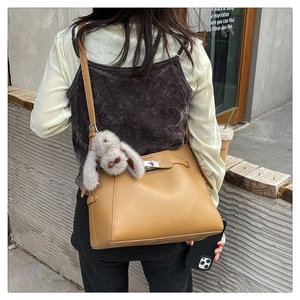 Close-up of a khaki lychee-textured bucket bag with silver lock and plush bunny charm