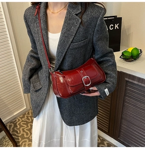 Detailed view of deep red patent leather handbag with silver buckle on grey blazer