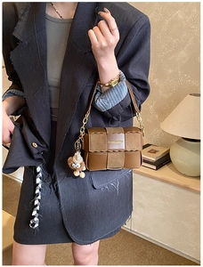 Detail of a brown woven shoulder bag with wavy edges and a plush doll pendant accessory