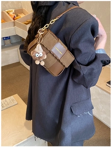 Detail of a brown woven crossbody bag with a gold chain and plush toy charm