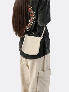 Minimalistische beige Umhängetasche aus genarbtem Leder mit schmalem Gurt am Model