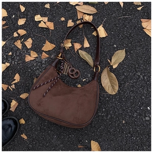 Detail of coffee suede crescent bag with leather trim on autumn leaves background