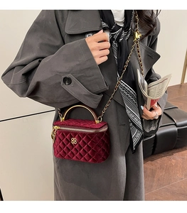 Detail of burgundy quilted velvet handbag with metal handle and clover emblem