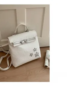Detail view of white pleated leather bag with silver star and bow charms on wood floor