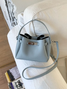 Light blue pebbled leather bucket bag with silver twist lock on a minimalist white sofa