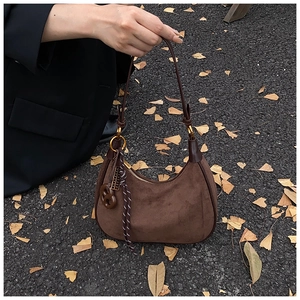Close-up of brown suede hobo bag with unique decorative charms on autumn leaf background