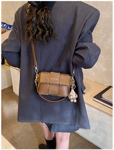 Detail of a brown woven leather crossbody bag with a plush monster charm and gold logo
