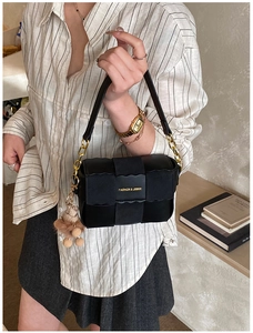 Detail of black leather handbag with scalloped edges, gold chain, and pompom charm