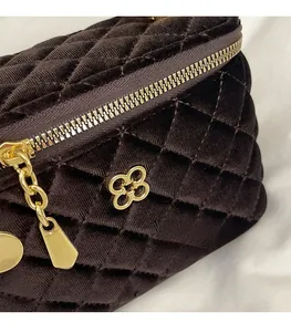 Detail of dark brown quilted velvet handbag with gold clover emblem and zipper