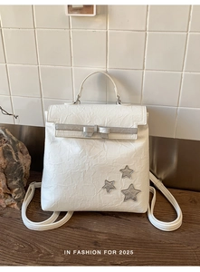 White backpack with crinkled texture, silver bow and star details in indoor setting