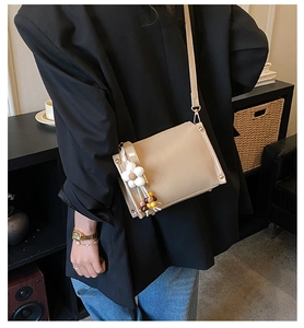 Detail of cream crossbody bag featuring delicate floral charms and fine shoulder strap