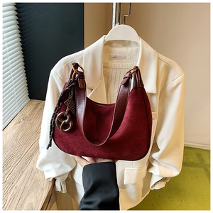 Detail of burgundy suede shoulder bag showing matte texture and woven pendant detail