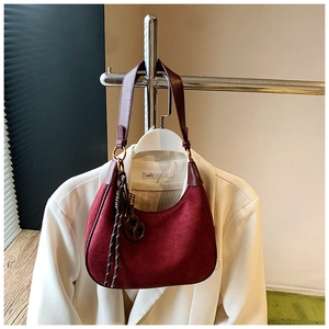 Close-up of deep red suede half-moon bag with woven detail hanging on a white blazer