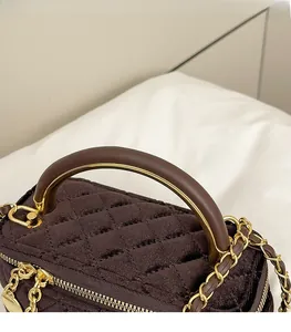 Close-up of brown quilted tweed handbag with leather handle and gold chain strap details