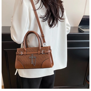 Detail of woven leather texture and silver cross pendant on a brown crossbody bag