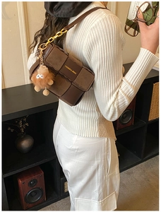 Brown woven checkerboard shoulder bag with gold chain and plush charm on white outfit