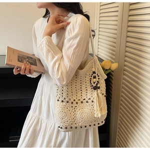 Détail d'un sac cabas tissé beige avec motifs ajourés, perles en bois et pompons