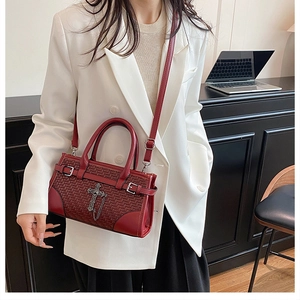 Close-up of woven wine red handbag with metal cross charm worn by a model in a modern office