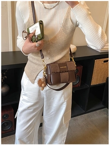 Detail of dark brown woven flap bag with gold chain and plush charm in a lifestyle setting