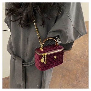 Detail of burgundy velvet quilted vanity bag with gold clover clasp and metal chain strap