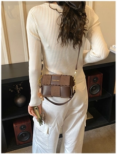 Detail of a vintage dark brown woven crossbody bag with a plush charm on a model