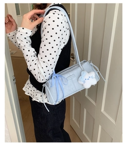 Detail of light blue shoulder bag featuring a plaid bow and white star cat plush pendant