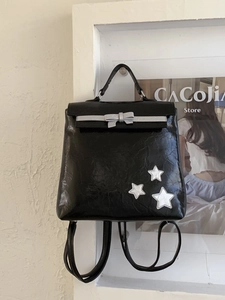 Glossy black pleated backpack with silver bow and star accents in a stylish setting